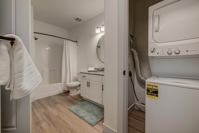 Modern apartment bathroom featuring a sleek granite countertop, integrated washer and dryer, and elegant laminate flooring.