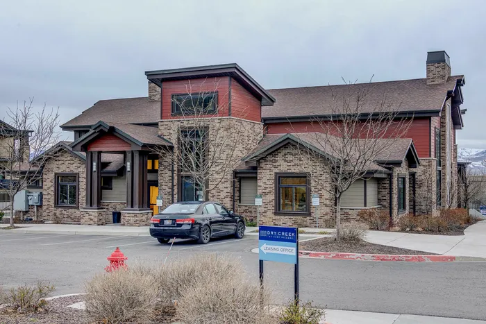 Charming brick and wood apartment building with stylish architecture, featuring a welcoming leasing office entrance and ample parking.