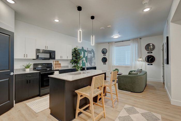 Modern open-concept kitchen and living room featuring sleek black and white cabinets, stylish pendant lighting, and a cozy seating area with world clocks.