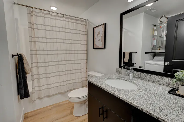 Sleek and modern bathroom featuring a granite countertop, stylish mirror, and a cozy shower with elegant fixtures.