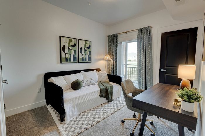 Charming home office with a cozy daybed, elegant artwork, and bright natural lighting through large windows, creating a perfect work-from-home environment.