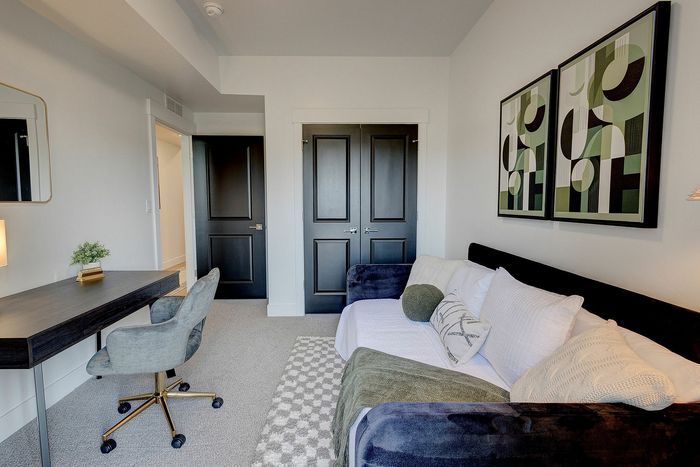 Modern home office featuring a comfortable grey chair, sleek dark wooden desk, plush couch with pillows, and abstract wall art.