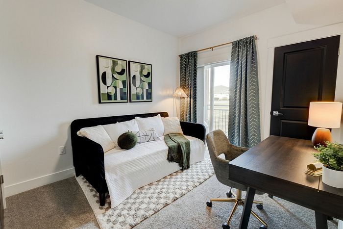 Chic home office with a cozy daybed, abstract wall art, and natural light streaming through floor-to-ceiling windows.