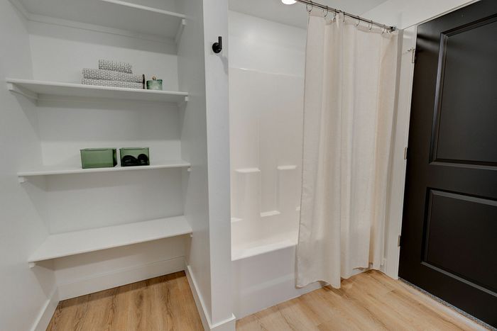 Modern bathroom with elegant wood flooring, built-in shelving, and a sleek shower with a beige curtain.