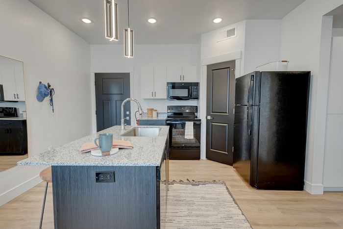 Modern apartment kitchen with sleek black appliances, elegant pendant lighting, and a chic granite-topped island.