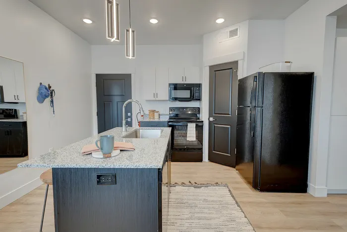 Modern kitchen with sleek black appliances, granite countertops, island seating, and stylish pendant lighting.