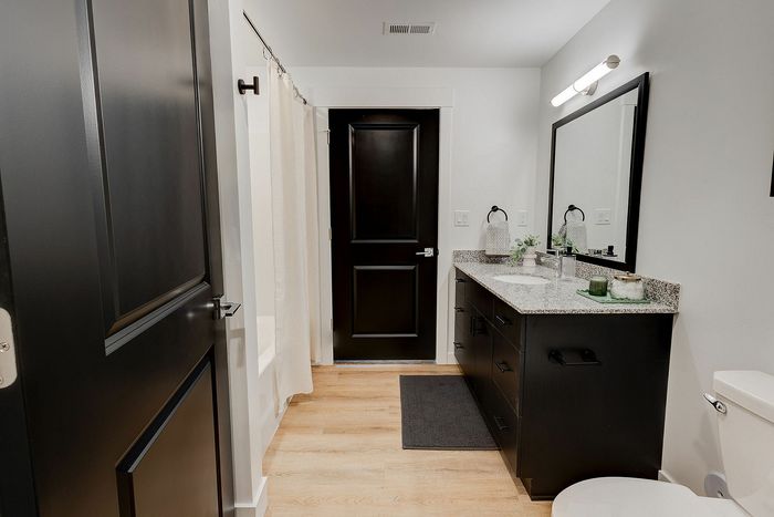 Elegant modern bathroom with sleek dark cabinetry, granite countertops, and contemporary lighting.