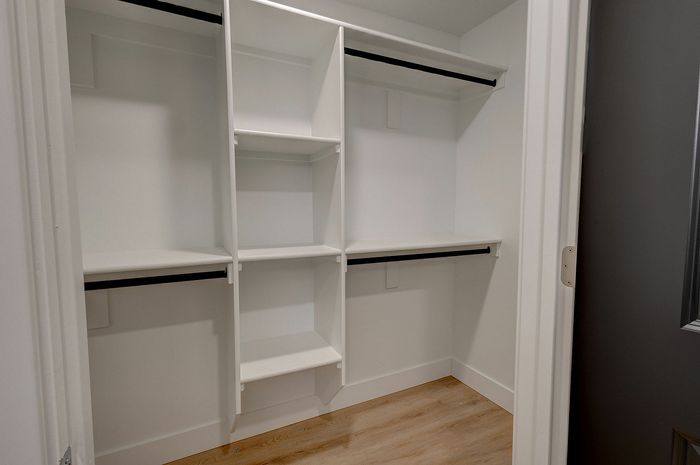 Spacious walk-in closet with sleek white shelving and ample hanging space, perfect for organized living.
