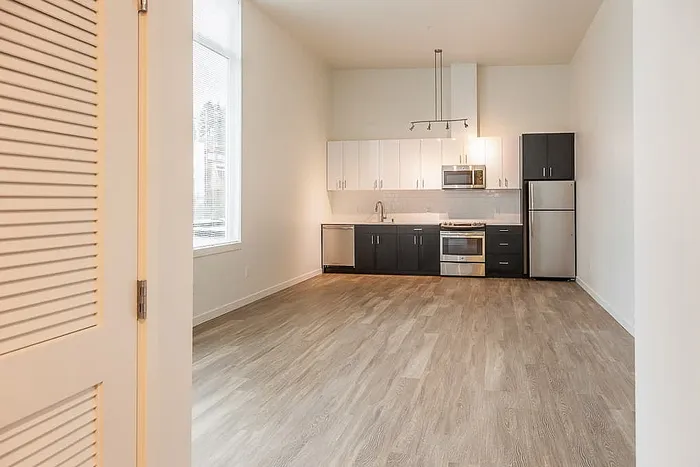 Modern kitchen with stainless steel appliances, stylish two-tone cabinetry, and elegant hardwood flooring, bathed in natural light from large windows.