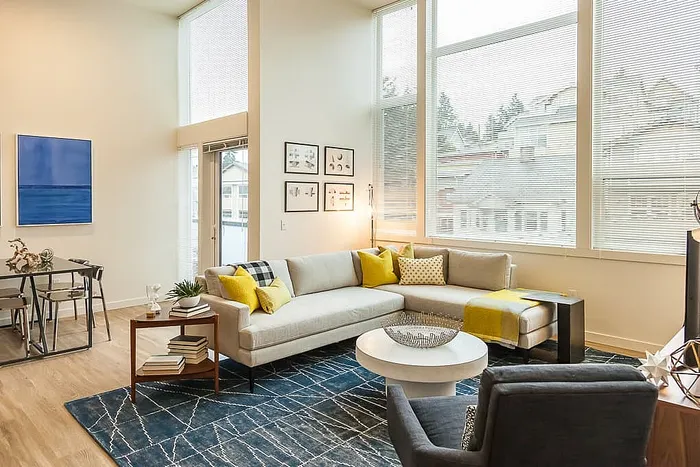 Bright and modern living room with high ceilings, featuring a stylish sectional sofa, large windows, and chic decor.