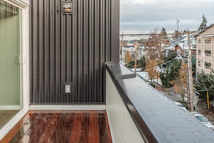 Charming apartment balcony with sleek metal siding, offering scenic views of a vibrant, tree-lined neighborhood and distant bridge.
