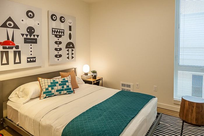 Cozy bedroom featuring modern abstract wall art, a stylish bed with vibrant cushions, and a warm, inviting ambiance.