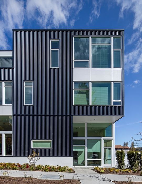 Modern architectural apartment exterior with sleek black facade and expansive windows, set against a bright blue sky.