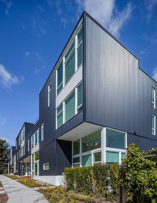 Modern architectural design showcasing a sleek, multi-story apartment building with large windows and elegant facade, set against a bright blue sky.
