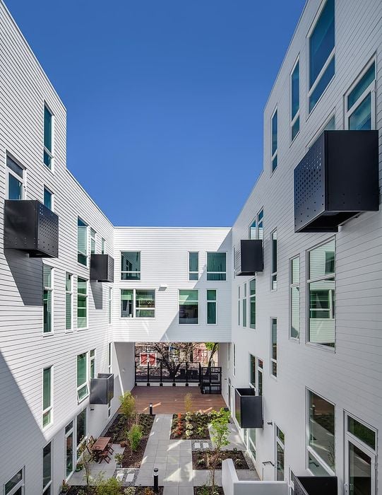 Modern apartment complex with sleek white exterior, large windows, and a beautifully landscaped courtyard.