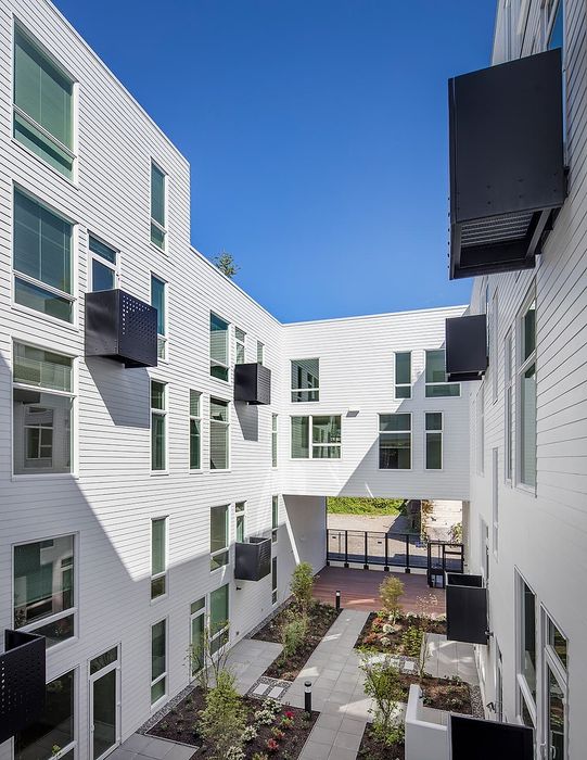 Modern apartment building courtyard with elegant white facade and lush greenery under a clear blue sky.