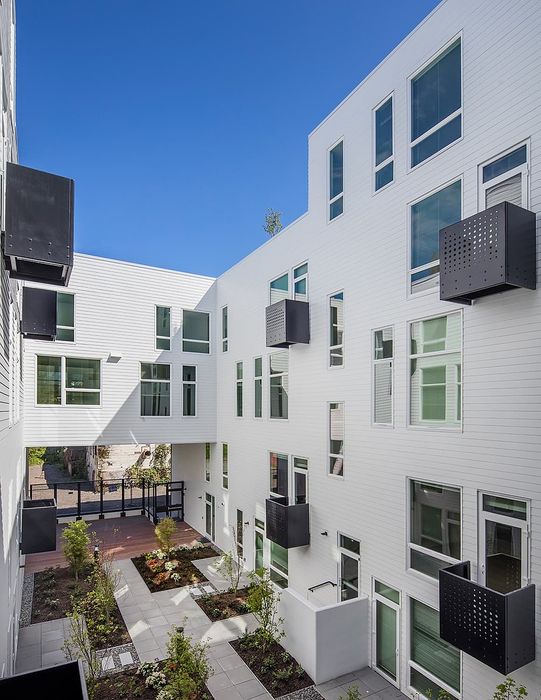 Modern apartment building with sleek white facade, large windows, and a beautifully landscaped courtyard for a sophisticated urban living experience.