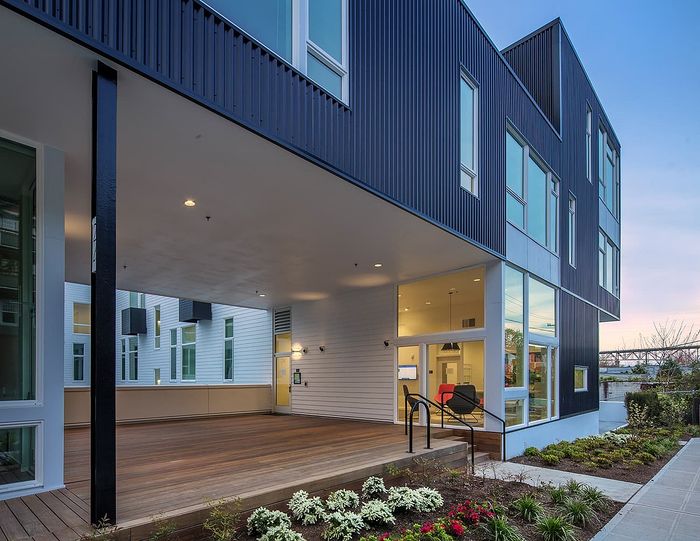 Modern apartment complex exterior showcasing sleek architecture, spacious covered deck, and landscaped entryway at sunset.