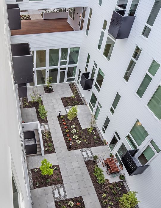 Elegant courtyard with lush garden beds and modern outdoor seating, surrounded by contemporary apartment design.