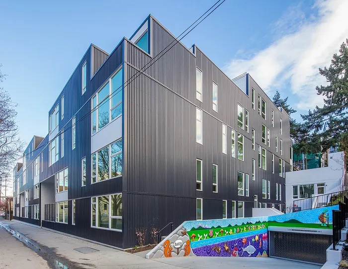 Modern apartment building with sleek black exterior and large windows, featuring vibrant artwork and lush greenery.