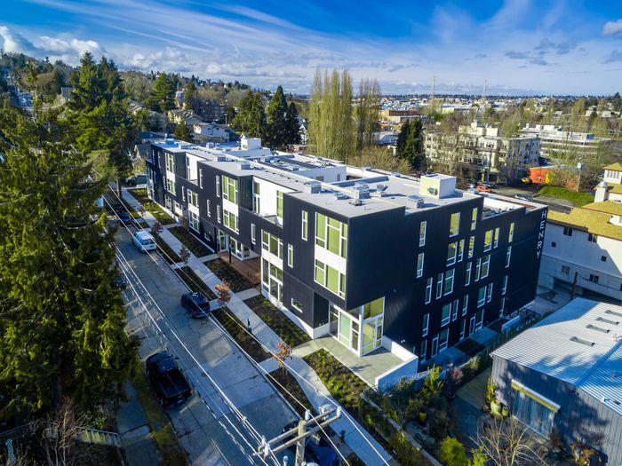 Modern apartment building with stylish black facade, surrounded by lush greenery and located in a scenic urban neighborhood.