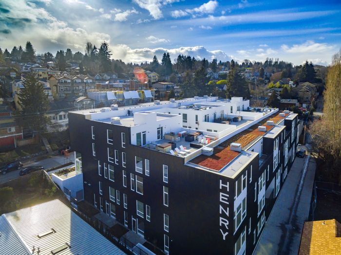 Contemporary urban apartment building with stunning rooftop views, set amidst a picturesque neighborhood with lush greenery and vibrant blue skies.
