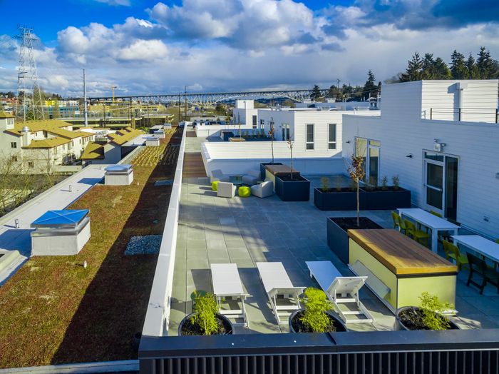 Spacious rooftop terrace with modern seating and greenery, offering stunning cityscape views under a vibrant blue sky.