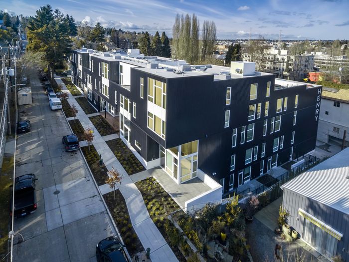 Modern apartment complex with sleek black facade, large windows, and landscaped pathways in a vibrant urban setting.