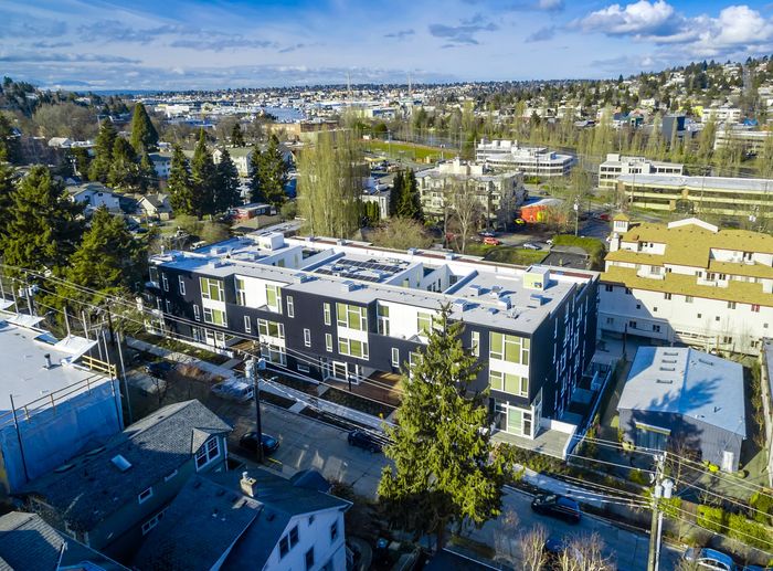 Captivating aerial view of a modern apartment building nestled in a vibrant neighborhood, surrounded by lush greenery and scenic cityscapes.