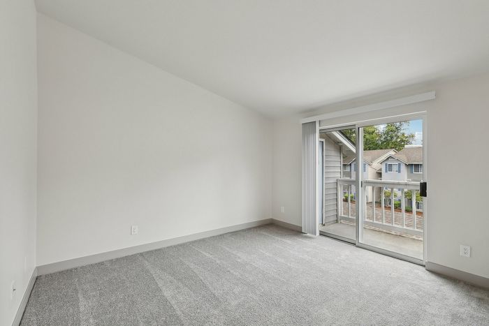 Bright and airy bedroom with plush carpet, large sliding glass doors, and a charming balcony view.