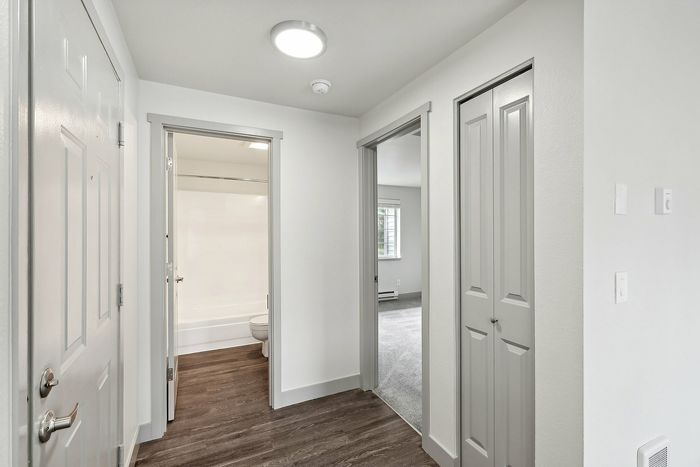 Modern apartment hallway with sleek wood flooring, bright white walls, and access to bathroom and bedroom.