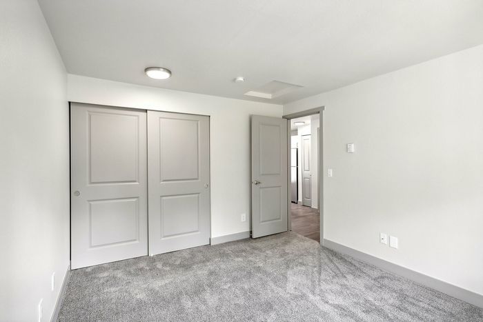 Bright and airy room with modern sliding closet doors, plush carpet, and sleek gray accents, offering a fresh canvas for your personal style.