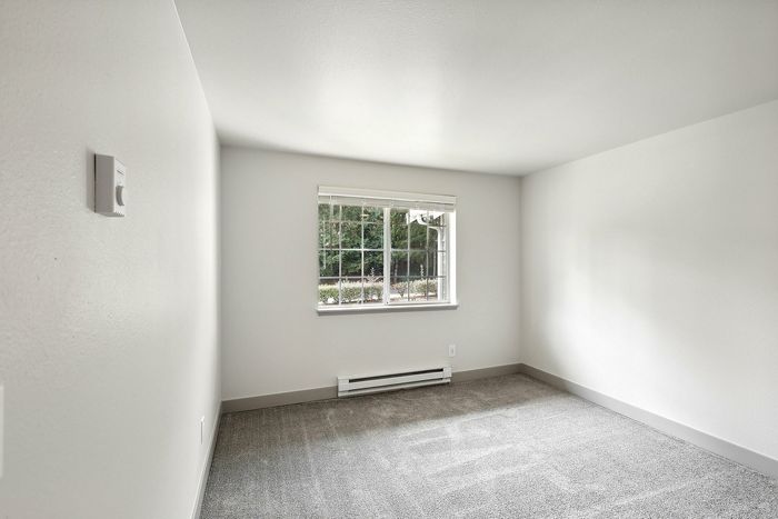 Bright and inviting room with large window, modern baseboard heating, and fresh neutral paint.