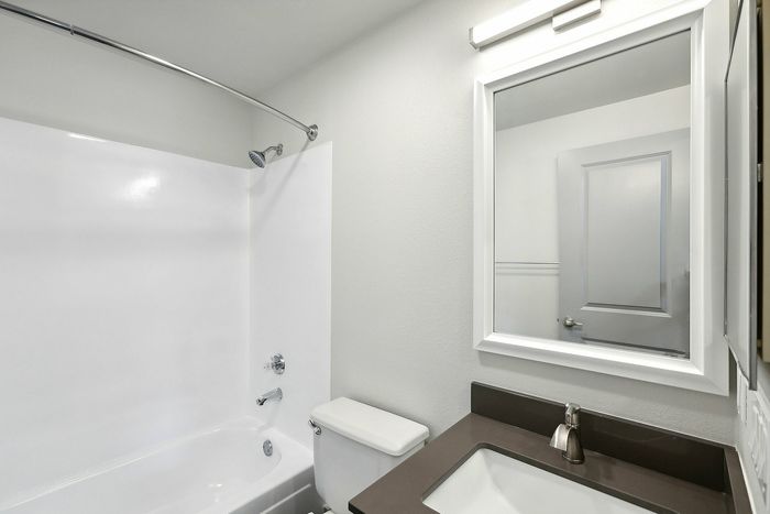 Modern bathroom with sleek design featuring a pristine bathtub, elegant sink, and glossy mirror under soft lighting.