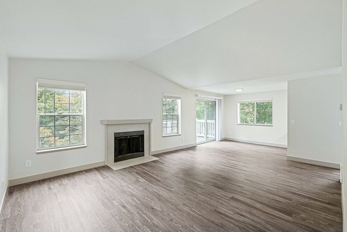 Bright and airy living room with elegant fireplace, large windows, and modern flooring overlooking lush greenery.
