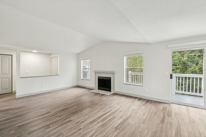 Bright, open living room with elegant hardwood floors, cozy fireplace, and access to a private balcony overlooking lush greenery.