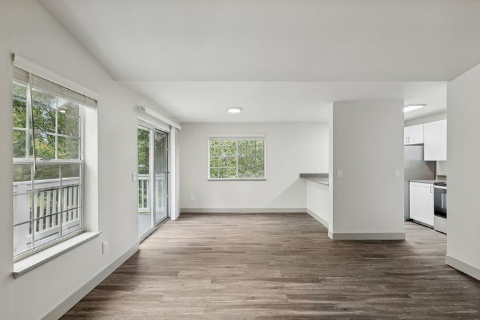 Bright, open living space with floor-to-ceiling windows, sleek wood flooring, and a modern kitchen, providing a seamless blend of style and functionality.