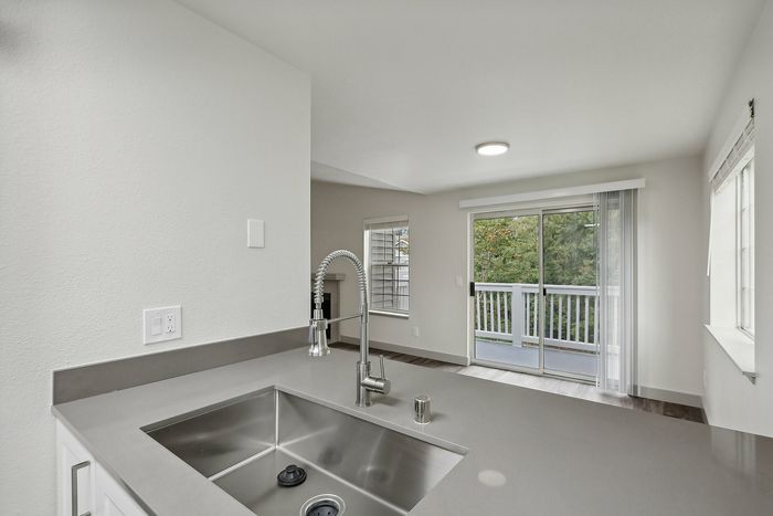 Modern kitchen with sleek silver sink and stylish faucet overlooking a bright living space with patio doors leading to a scenic balcony view.