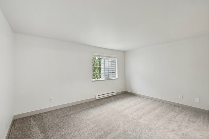 Bright and spacious room with plush carpet and a large window bringing in natural light, ideal for a cozy bedroom or inviting home office.