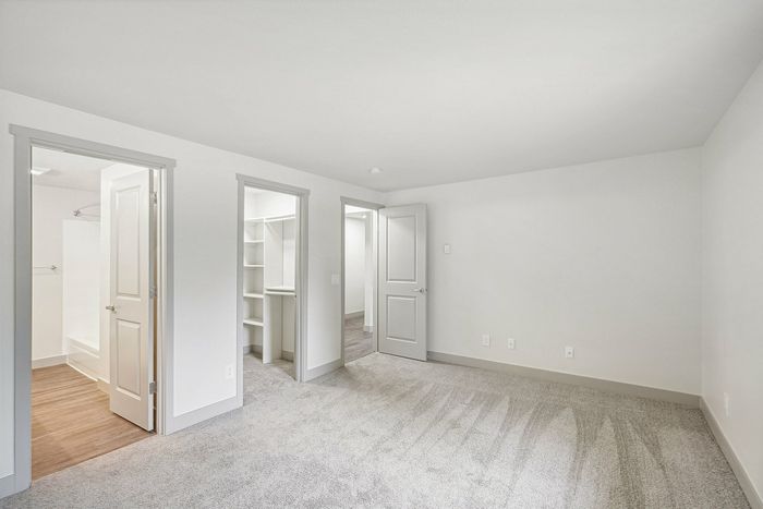 Spacious bedroom with plush carpeting and walk-in closet, featuring a stylish neutral palette and elegant doorways.