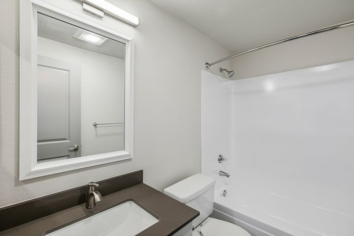 Modern bathroom featuring sleek vanity with integrated sink, polished mirror, and pristine bathtub with shower amenities.