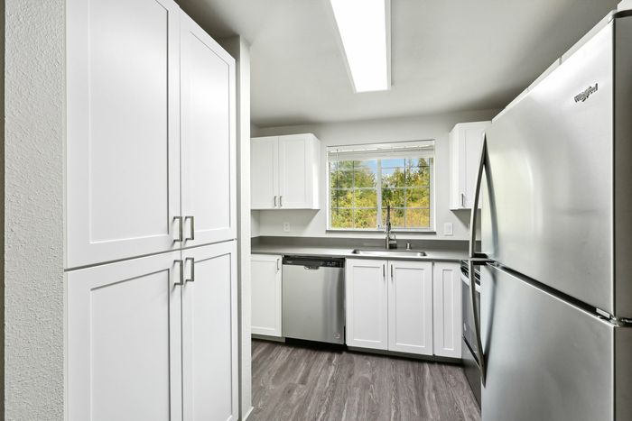 Bright and modern kitchen with sleek stainless steel appliances, elegant white cabinetry, and a serene view from the window.