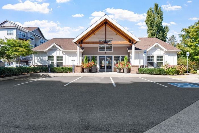 Inviting apartment complex entrance with beautiful landscaping and ample parking under a bright blue sky.