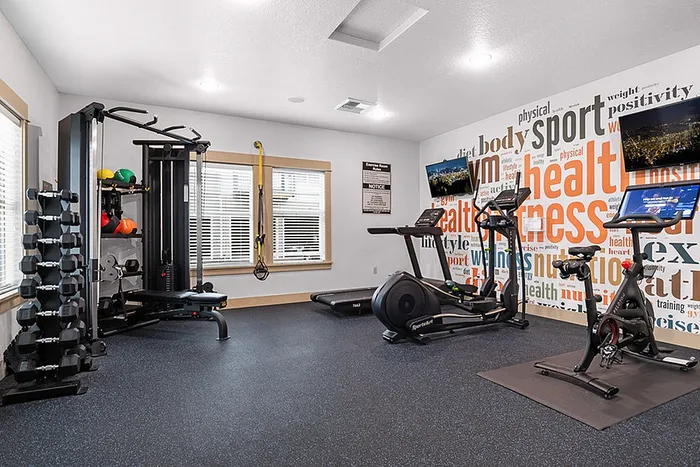 Modern apartment gym featuring sleek exercise machines, motivational wall art, and ample natural light.