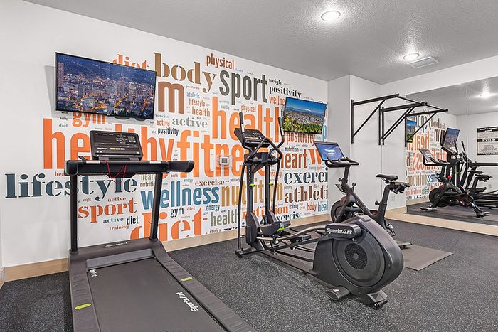 Modern fitness room with state-of-the-art exercise equipment, motivational wall graphics, and mounted TV for an engaging workout experience.
