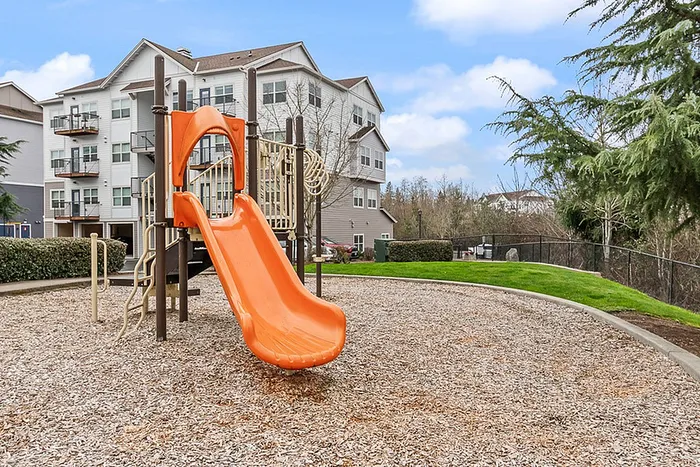 Inviting playground with vibrant orange slide set in a picturesque community surrounded by modern apartments and lush greenery.