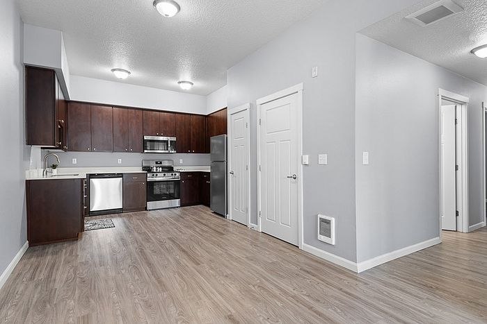 Modern kitchen with sleek stainless steel appliances, rich wooden cabinetry, and elegant gray walls complementing light wood flooring.