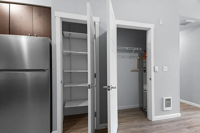Modern apartment kitchen with sleek stainless steel refrigerator, spacious pantry, and utility closet for convenient storage solutions.