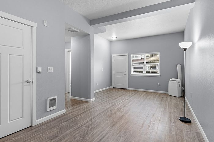 Spacious and modern living area with elegant wood flooring, light gray walls, and ample natural light.