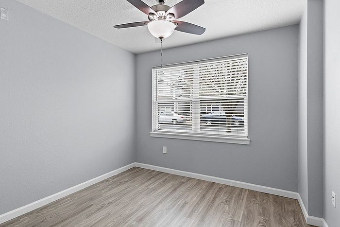 Bright and spacious room with modern gray walls, sleek gray flooring, and a large window offering natural light, perfect for a cozy bedroom or home office.